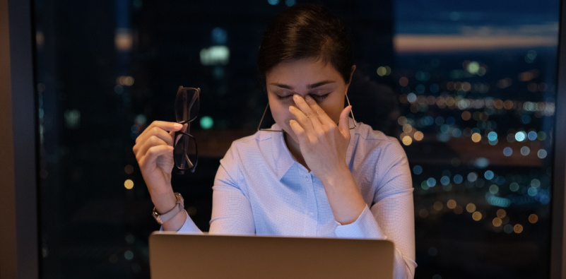 A woman sitting at a desk with a laptop and glasses, showing our Relax Lens Special to combat digital eye strain